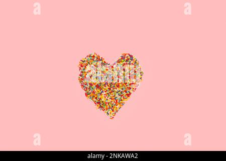 Sweet colored sprinkles in heart shape on a pink background with copy space Stock Photo
