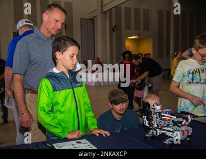 U.S. Marine Corps Col. Brendan C. Burks, Marine Corps Air Station Cherry Point commanding officer, and his son observe robots at the Fleet Readiness Center East's robotics table during the 11th Annual Fly-In Family Movie and STEM Night at the Havelock Tourist and Event Center, Havelock, North Carolina, Aug. 12, 2022. ECAHF affords local youth the opportunity to learn more about science, technology, engineering, and math through demonstrations and interactive activities. DOTMIL,FamilyFly-In,dvids,mcasCherryPoint, Stock Photo