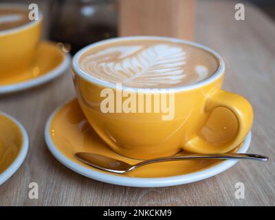 Yellow cup of cappuccino or latte on the table in the cafe, close up. Ceramic cup of hot coffee, selective focus Stock Photo
