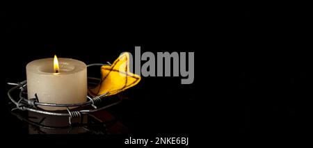 Burning candle, barbed wire and Jewish badge on dark background with space for text. International Holocaust Remembrance Day Stock Photo