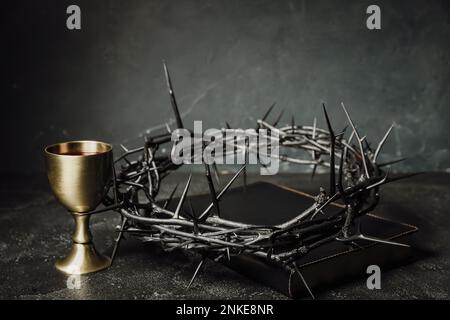 Crown of thorns with Holy Bible and cup of wine on dark background Stock Photo