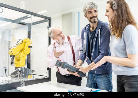 Colleagues watching woman programming robot arm with digital control Stock Photo