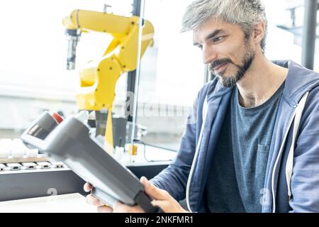 Skilled worker in robotic factory controlling robot arm with digital control Stock Photo