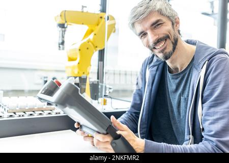 Skilled worker in robotic factory controlling robot arm with digital control Stock Photo