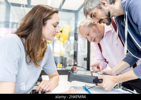 Colleagues watching woman programming robot arm with digital control Stock Photo