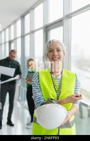Smiling woman wearing protective workwear with colleagues in background in office Stock Photo