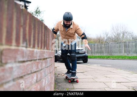 Mature man learning skateboarding taking support of wall on footpath Stock Photo