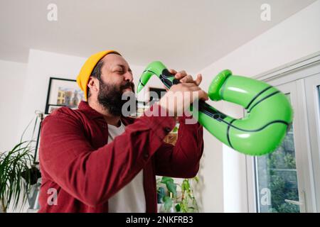Happy man playing with inflatable saxophone at home Stock Photo