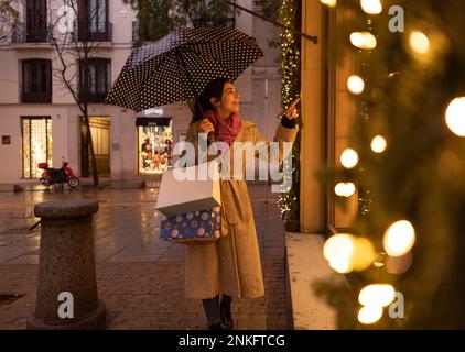 Smiling young woman gesturing and doing window shopping at footpath Stock Photo