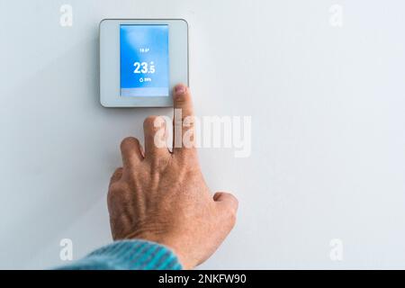 Hand of man adjusting thermostat on wall Stock Photo