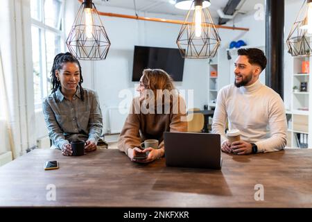 Happy coworkers sitting together having coffee in cafeteria Stock Photo