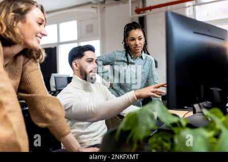 Young businessman explaining colleagues using desktop PC at office Stock Photo