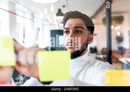 Young businessman sticking adhesives notes on glass Stock Photo