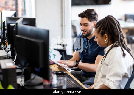 Young businessman and businesswoman working on charts at desktop PC in office Stock Photo