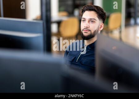 Thoughtful young businessman sitting at desktop PC in office Stock Photo