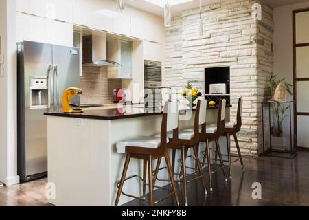 Kitchen with white lacquered wooden cabinets, island with quartz countertop and high back barstools, recessed toaster and wine rack. Stock Photo