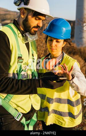 Engineer using smart phone with technician on sunny day Stock Photo