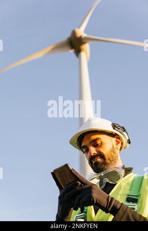 Technician using smart phone in front of wind turbine Stock Photo
