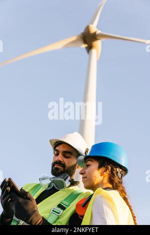 Engineer with technician using smart phone in front of wind turbine Stock Photo