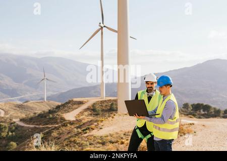 Technician and engineer working on laptop in front of wind turbines Stock Photo