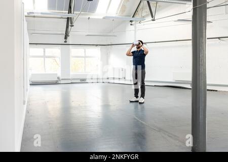 Young businessman wearing VR glasses standing in empty office Stock Photo