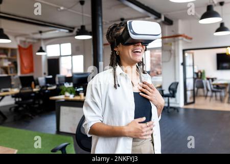 Happy businesswoman wearing VR glasses standing in office Stock Photo