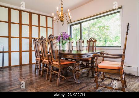 Dining room with 14th century antique wood table and high back grid chairs inside contemporary home. Stock Photo