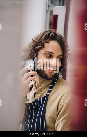 Smiling young businessman talking over smart phone leaning on van Stock Photo
