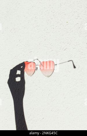 Shadow of hand holding heart shape sunglasses on wall Stock Photo