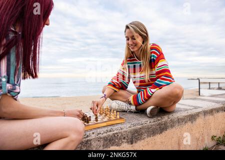 Happy friends playing chess on wall at promenade Stock Photo