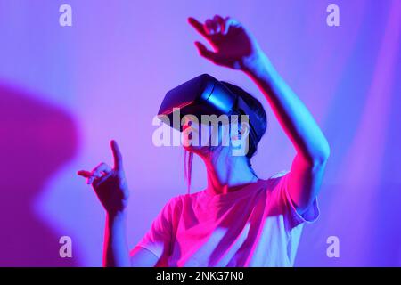 Woman watching VR Goggles and gesturing against colored background Stock Photo