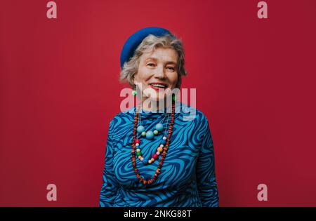 Happy senior woman wearing jewelry against red background Stock Photo