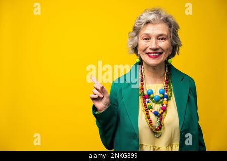 Smiling senior woman pointing against yellow background Stock Photo
