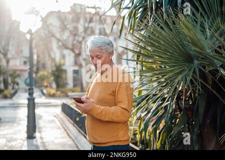 Senior man using smart phone standing at footpath Stock Photo