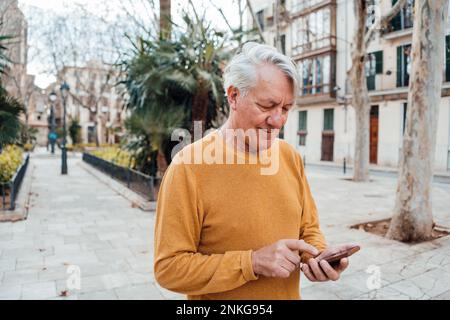 Senior man using smart phone at footpath Stock Photo