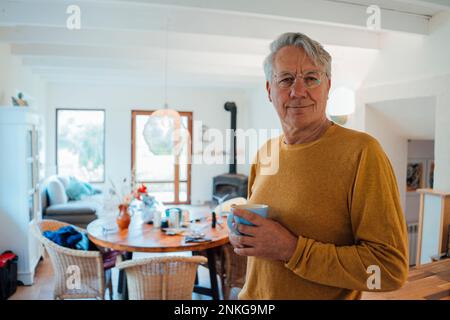 Smiling senior man standing with coffee cup at home Stock Photo