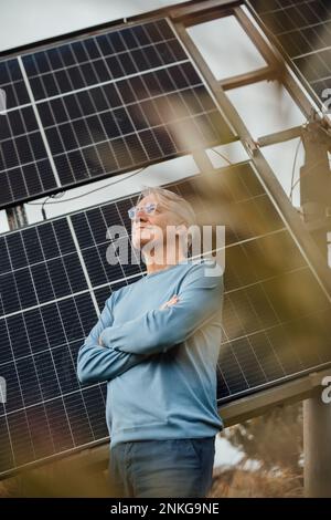 Smiling man standing with arms crossed standing by solar panels Stock Photo