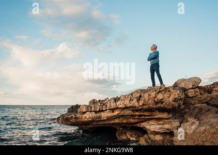 Senior man standing with arms crossed on rock Stock Photo