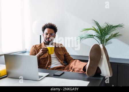 Businessman with coffee cup sitting at desk in front of wall Stock Photo