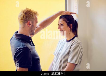 Happy young man measuring height of woman at home Stock Photo