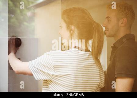 Young couple adjusting thermostat seen through glass Stock Photo