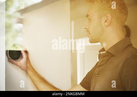 Young man adjusting thermostat seen through glass Stock Photo