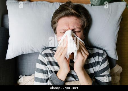 Man blowing nose in napkin lying on bed Stock Photo