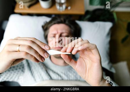 Man looking at thermometer lying on bed at home Stock Photo