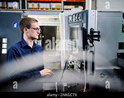 Technician using laptop at machine in modern factory Stock Photo