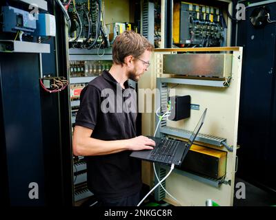 Technician using laptop at machine in modern factory Stock Photo