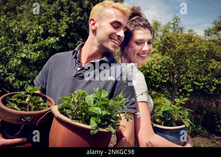 Happy couple standing back to back holding potted plants Stock Photo
