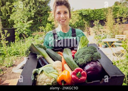 Smiling young delivery person with box of fresh vegetables Stock Photo