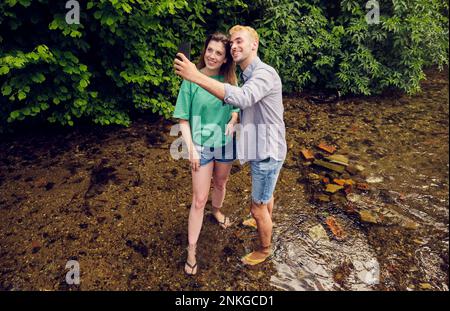 Young couple taking selfie through smart phone standing in stream Stock Photo