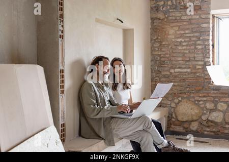 Happy mature man using laptop with woman holding documents Stock Photo